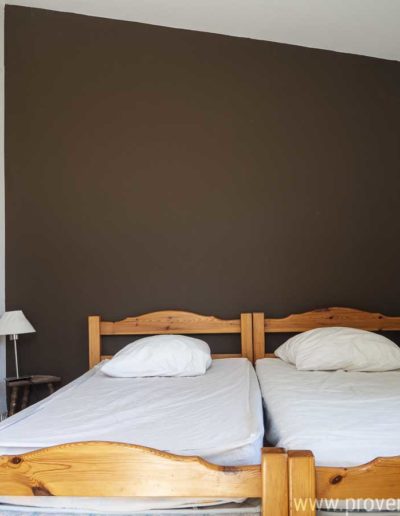 La chambre enfant avec ses deux lits une place, sa décoration épuré et l'accès aux sanitaires par la porte en bois sur la gauche. Les Gavottes est une maison de vacances familiale située au Revest des Brousses, en Provence.