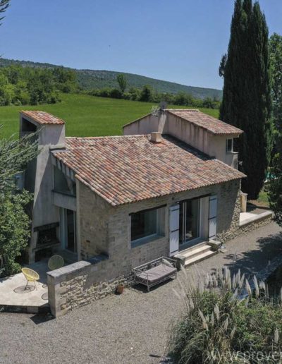 Vue du ciel de la façade principale à l'ouest et ses ouvertures panoramiques sur le jardin, puis la terrasse côté nord et son barbecue en dur permettant l'accès à la maison par une large baie vitrée coulissante apportant une belle luminosité à l'intérieur de la location de vacances Les Gavottes située au Revest des Brousses en Provence.