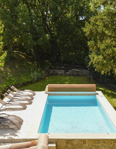 La piscine avec son eau cristalline et sa plage en pierre équipée de transat entourée d'une nature verdoyante et d'arbres majestueux pour un confort et une intimité totale au cœur de la location de vacances Les Gavottes, située au Revest des Brousses, en Provence.