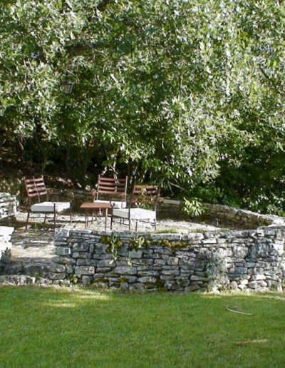 A l'ombre d'un arbre majestueux, niché au cœur d'une restanque en pierre, un espace cosy équipé d'un salon d'extérieur comme un cocon au fond du jardin ou l'on peut admirer la vue et se délecter du calme absolu pour un séjour en mode détente au sein de la location de vacances Les Gavottes, au Revest des Brousses, en Provence.