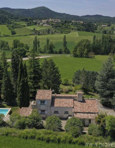 Vue aérienne de la maison et son environnement verdoyant avec la multitude d'arbres entourant la maison pour apporter ombre et fraicheur et en panoramique le village pittoresque et les champs à perte de vue. La maison de vacances Les Gavottes est située sur la commune du Revest des Brousses, au calme absolu, sans vis à vis pour profiter de la nature provençale.