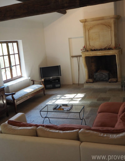 Le salon avec son large canapé confortable, sa cheminée en pierre et son mobilier en bois apporte tout le charme à la location de vacances La Poncette à Reillanne en Luberon