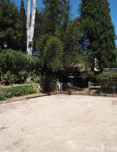 Le grand terrain de boule ensoleillé, entouré d'arbre et de végétation pour des parties de pétanque en famille ou entre amis au sein de la location de vacances Le Castellas située à Manosque dans le Luberon.