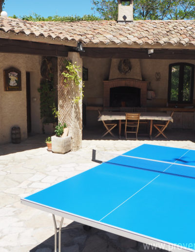 La terrasse extérieur baignée de soleil avec la table de ping-pong et une partie couverte abritant la cuisine d'été avec son barbecue et son espace repas permettant les belles tablées lors des douces nuits d'été dans la location de vacances Le Castellas à Manosque au cœur du Luberon.