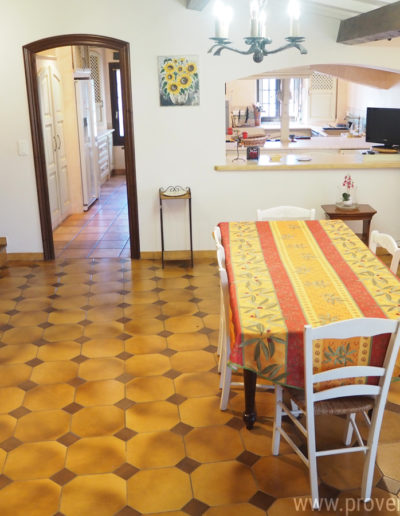 L'espace repas équipée d'une table pouvant recevoir jusqu'à 8 personnes et sa vue sur la cuisine par le large passe plat, alliant charme et authenticité avec ses poutres en bois et son lustre en fer forgé pour des vacances agréables dans la location de vacances Le Castellas située à Manosque au cœur du Luberon.