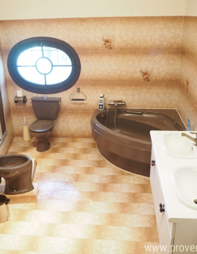 La salle de bain fonctionnelle et bien équipée, se compose d'un meuble blanc double vasque, une large baignoire d’angle, un bidet, un WC et une douche dans un décor année 70 baigné de lumière par sa fenêtre ovale originale. Le confort assuré dans la location de vacances Le Castellas située à Manosque dans le Luberon.