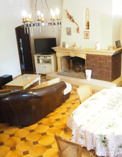 L'espace salon disposant d'un écran télé, avec son large canapé pouvant accueillir plusieurs personnes, sa cheminée en pierre et la décoration sobre alliant le bois, la pierre et le lustre en fer forgé qui apporte tout son cachet à la location de vacances Le Castellas située à Manosque dans le Luberon.