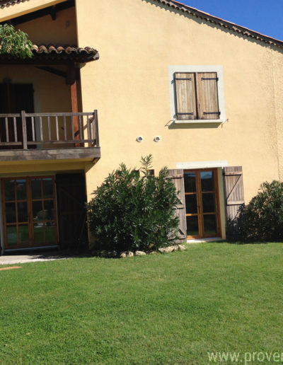 La façade sud avec ses grandes baies vitrées au rez-de-chaussée, la terrasse couverte et le joli balcon en bois du T4 à l'étage de la location de vacances Les Lavandins située à Lurs au coeur de la Provence.