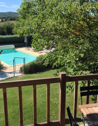 La vue sur la piscine baignée de soleil dans son écrin de verdure, depuis le joli balcon en bois du T4 de la location de vacances Les Lavandins située à Lurs en Provence.