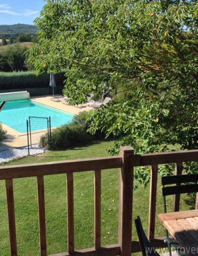 La vue sur la piscine baignée de soleil dans son écrin de verdure, depuis le joli balcon en bois du T4 de la location de vacances Les Lavandins située à Lurs en Provence.