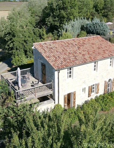 Vue du ciel sur la façade baignée de soleil de la Santoline avec sa terrasse en bois au cœur du jardin verdoyant du domaine de 