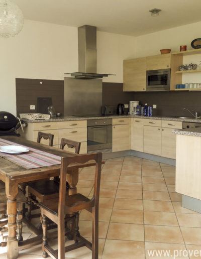 L'espace cuisine entièrement équipée et aménagée avec de nombreux rangement et une belle table en bois avec ses chaises assorties pour des repas conviviaux au sein de la location de vacances Le Fontauris au cœur de Forcalquier, en Provence.