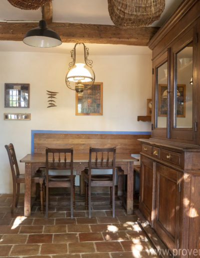 La cuisine avec son espace repas et son grand vaisselier en bois, les poutres apparentes, les panier en osier, chaleur et convivialité au sein de la location de vacances La Norgère à Mane en Provence.