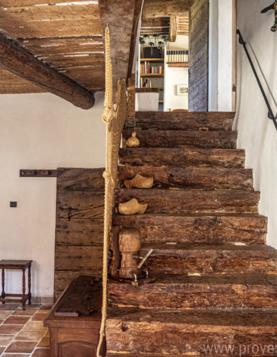 L'escalier en bois brute avec sa main courante en fer forgé et le garde corps en macramé et sur le côté le plafond de l'espace bureau avec ses poutres apparentes. Un lieu authentique et plein de charme, tel et l’ADN du gîte de vacances La Norgère à Mane en Provence.