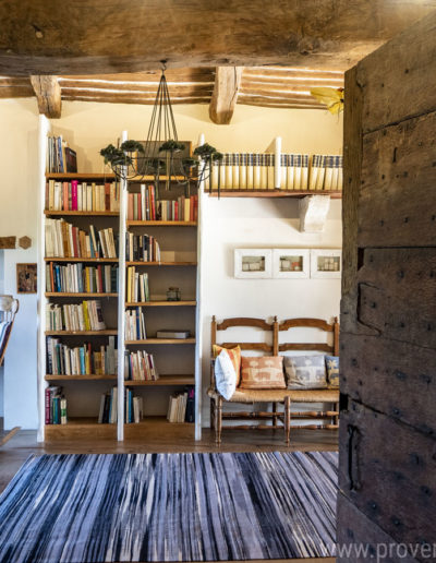 La belle porte en bois ouvrant sur le salon et révélant l'espace bibliothèque avec ses étagères en bois et cet authentique plafond à la française avec poutres apparentes font le charme de la location de vacances La Norgère situé à Mane au cœur de la Provence.