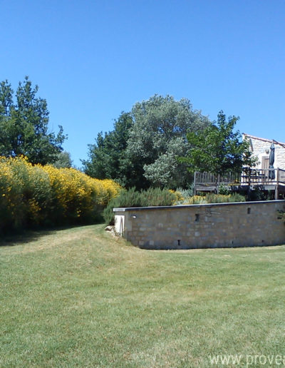 La terrasse en bois côté sud baignée de soleil surplombant le jardin végétalisé et joliment entretenu de la location de vacances La Santoline, située à Lurs en Provence.