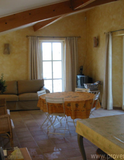 Le salon au couleur provençale avec ses murs jaune soleil, le charme des poutres apparentes et le mobilier confortable pour des vacances apaisantes dans la location La Santoline située à Lurs au coeur de la Provence.