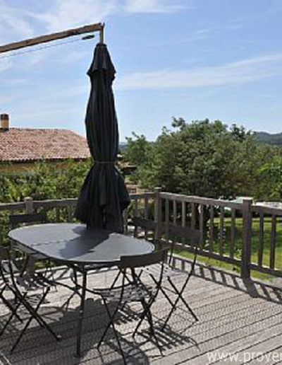 La terrasse en bois ensoleillée surplombant le jardin du domaine de la location de vacances La Santoline à Lurs en Provence.