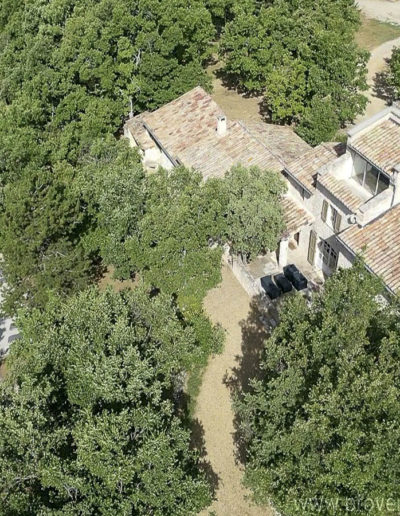Vue aérienne du jardin arboré, la piscine avec son eau cristalline et la bâtisse en pierre composant la location de vacances La Poncette au coeur du Luberon dans le joli village de Reillanne