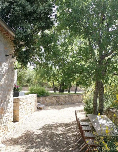 L'espace repas extérieur ombragé par la végétation luxuriante et la façade en pierre authentique de la location de vacances La Poncette située à Reillanne dans le Luberon.