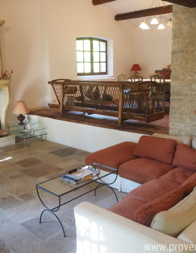 Un grand espace salon avec sa cheminée authentique en pierre et son grand canapé confortable en contrebas de l'espace salle à manger. Une décoration style campagne rehaussée par le charme de la pierre et des poutres apparentes pour cette location de vacances La Poncette située à Reillanne dans le Luberon.