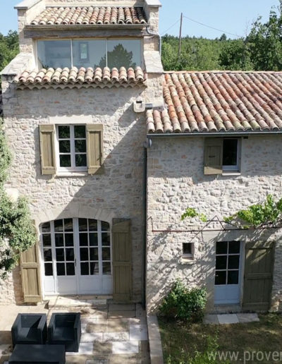 Vue de face de la façade principale en pierre et ses portes-fenêtres croisillon donnant tout son cachet à la location de vacances La Poncette située dans le joli village de Reillanne en Luberon.