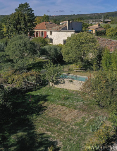 Le jardin arboré et ombragé avec la piscine à l'eau turquoise et le charme de la façade en pierre de la locations de vacances La Norgère au cœur de la Provence à Mane.