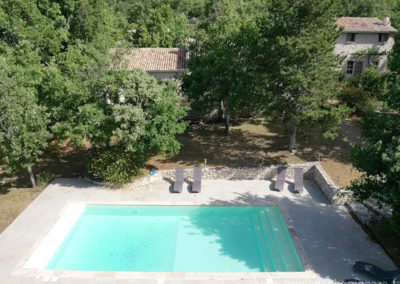 Vue aérienne de la piscine avec vue de la maison à travers les arbres, transats, terrain arboré et ombragé dans le Luberon, grande maison gérée par Provence Home Care